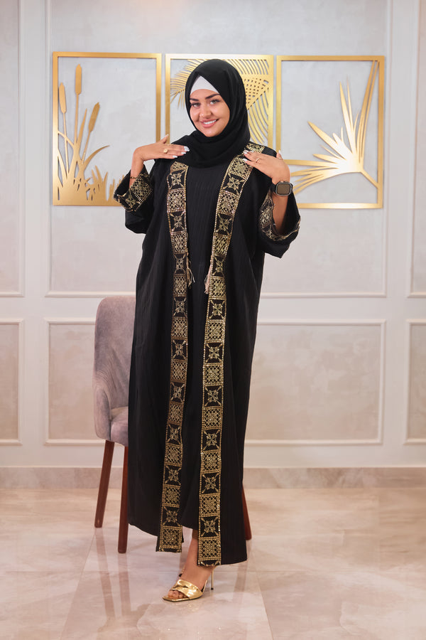 Woman wearing a black abaya with gold embroidery in a decorated room.
