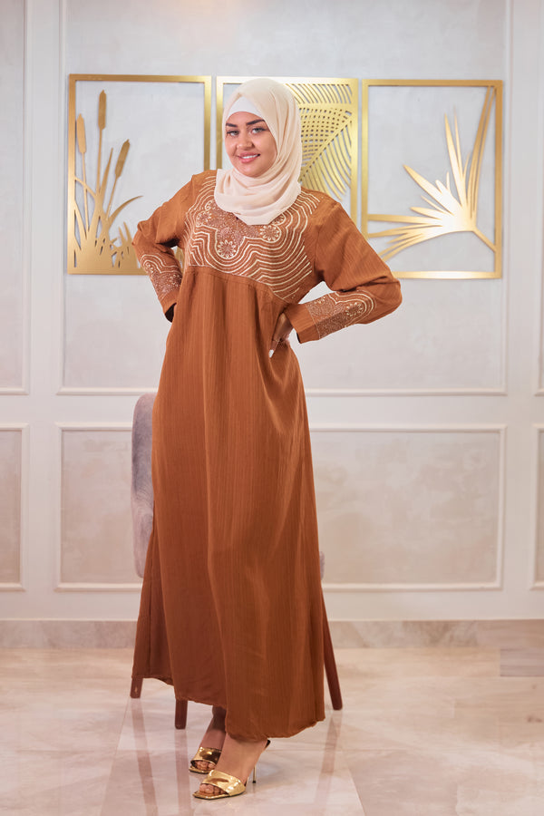 Woman wearing a brown dress with gold embroidery in a decorated room.